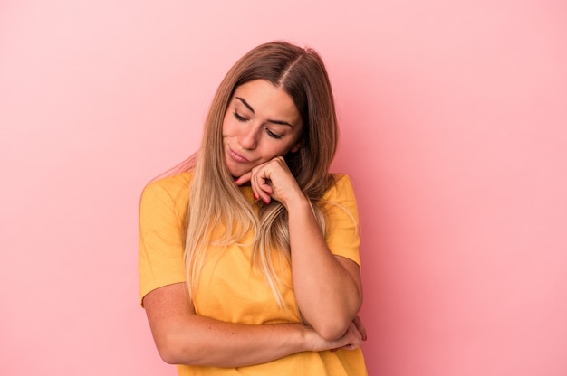 Giovane donna russa isolata su sfondo rosa guardando lateralmente con espressione dubbiosa e scettica.