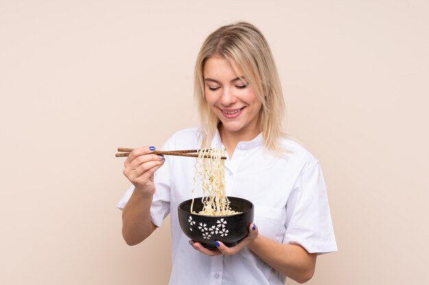 Giovane donna russa sopra la parete isolata che tiene una ciotola di tagliatelle con le bacchette