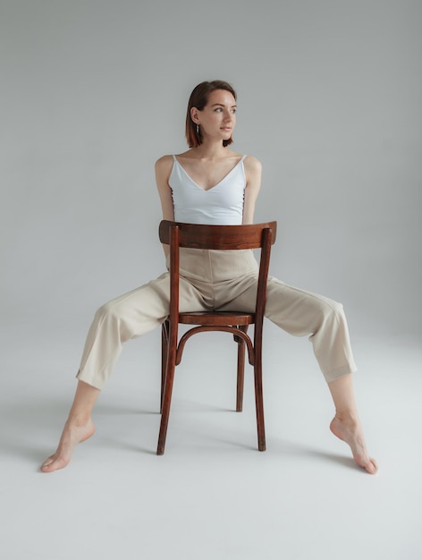 Giovane donna scalza e sciolta si siede su una sedia di legno in uno studio grigio Lifestyle Fashion snapshot