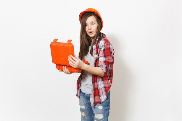 Giovane donna scioccata in abiti casual e elmetto protettivo che tiene la custodia aperta con strumenti o cassetta degli attrezzi isolata su sfondo bianco. Strumenti, strumenti per la ristrutturazione della stanza. Riparare il concetto di casa.