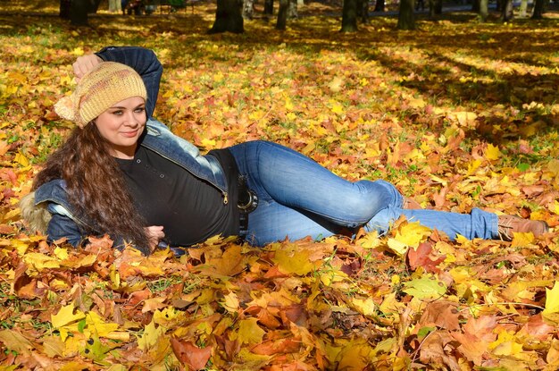 Giovane donna sdraiata in foglie autunnali luminose e sorridente