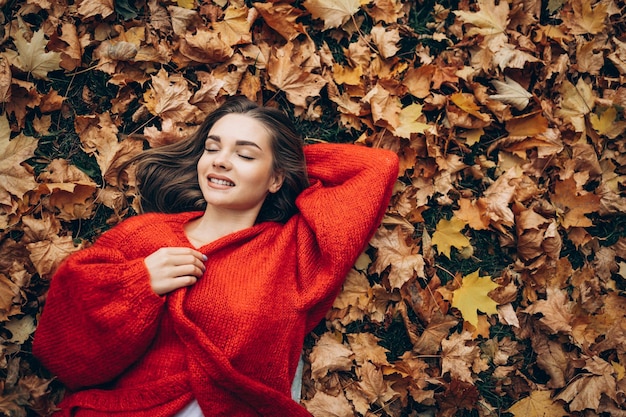 Giovane donna sdraiata nel parco sull'erba in foglie d'autunno