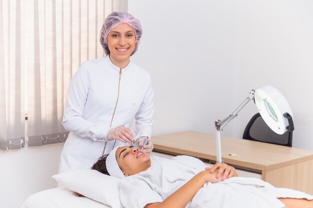 Giovane donna sdraiata sul tavolo del cosmetologo durante la procedura di ringiovanimento. Il cosmetologo si prende cura della giovinezza e del benessere della pelle del collo e del viso. Procedura di pulizia del viso dell'hardware.