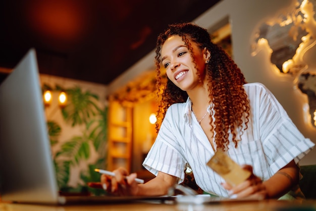 Giovane donna seduta al bar che fa shopping online utilizzando carta di credito e laptop Shopping online