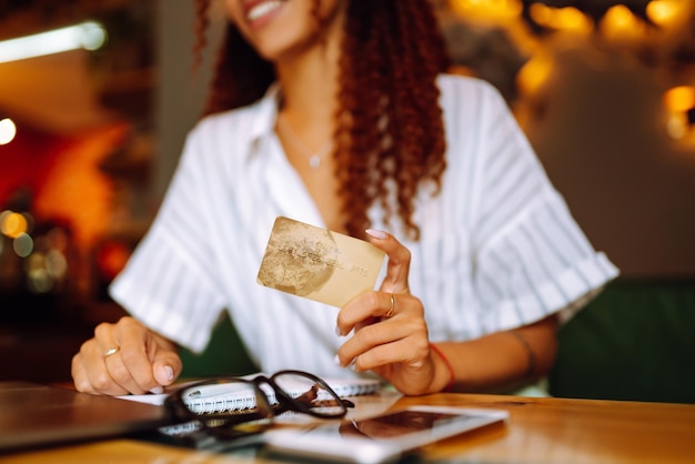 Giovane donna seduta al bar che fa shopping online utilizzando carta di credito e laptop Shopping online