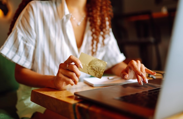 Giovane donna seduta al bar che fa shopping online utilizzando carta di credito e laptop Shopping online