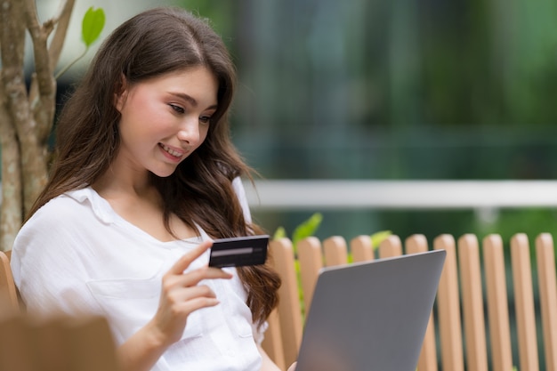 Giovane donna seduta con faccina sorridente utilizzando laptop con tenendo la carta di credito presso il centro commerciale