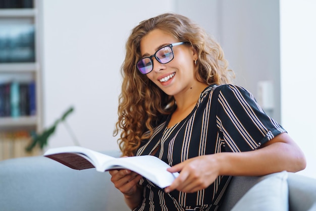 Giovane donna seduta con un libro portatile in biblioteca e prendere appunti di apprendimento Concetto di educazione