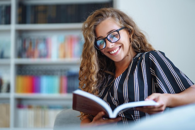 Giovane donna seduta con un libro portatile in biblioteca e prendere appunti di apprendimento Concetto di educazione