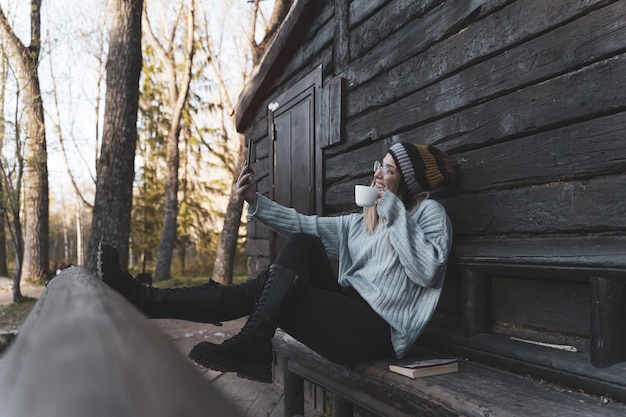 Giovane donna seduta davanti alla cabina di legno che si fa un selfie