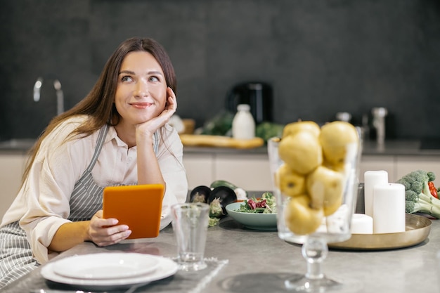 Giovane donna seduta in cucina e guardando pensierosa