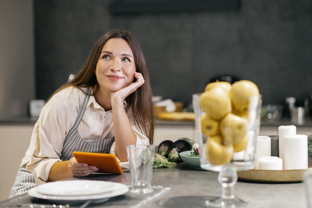 Giovane donna seduta in cucina e guardando pensierosa