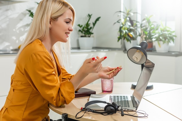 Giovane donna seduta in cucina e lavorando sul computer portatile.