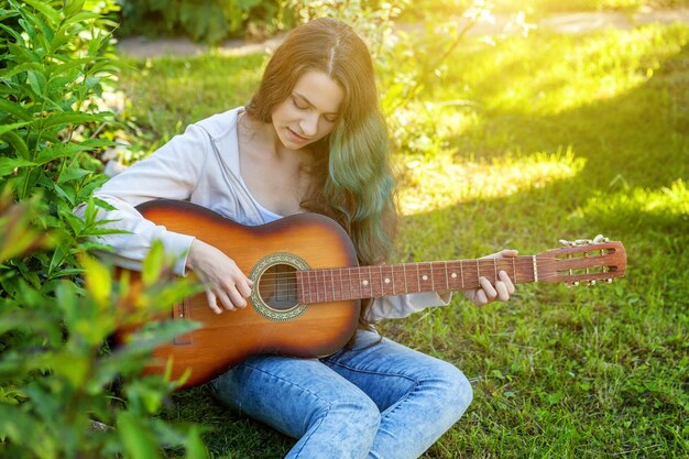 Giovane donna seduta in erba e suonare la chitarra