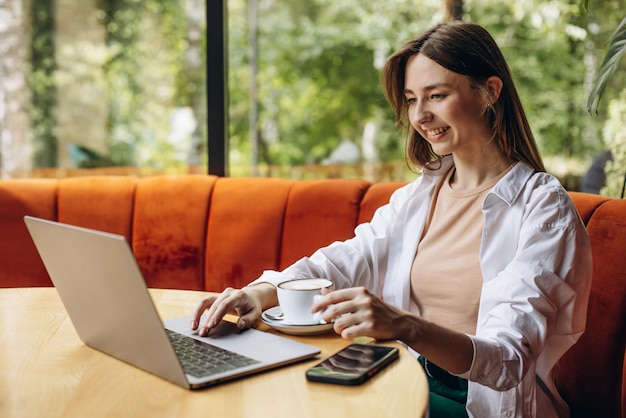 Giovane donna seduta in un caffè che beve caffè e lavora al computer