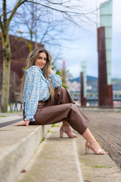 Giovane donna seduta in un parco della città concetto di stile di vita sorridente camicia blu e pantaloni marroni