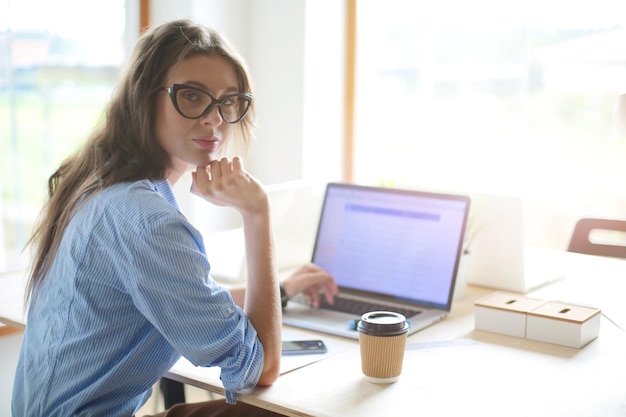 Giovane donna seduta nella tabella dell'ufficio guardando lo schermo del computer portatile Giovane donna