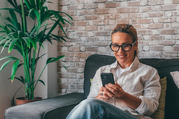 Giovane donna seduta rilassarsi sul divano in soggiorno navigando navigando in internet wireless su smartphone ragazza millenaria riposa sul divano a casa testo del messaggio sul cellulare moderno shopping online tramite websitexA