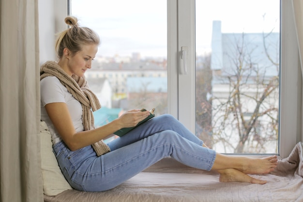 Giovane donna seduta su un davanzale e leggere libri interessanti