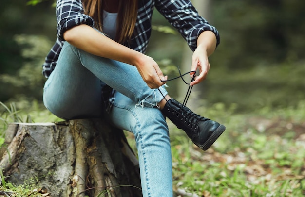 Giovane donna seduta sul ceppo con la foresta verde sullo sfondo e legare i lacci delle scarpe sugli scarponi da trekking