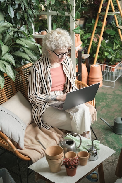 Giovane donna seduta sul divano con il computer portatile sulle ginocchia e scrivendoci sopra lavora in giardino