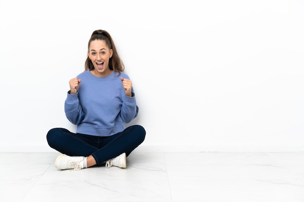 Giovane donna seduta sul pavimento che celebra una vittoria nella posizione del vincitore