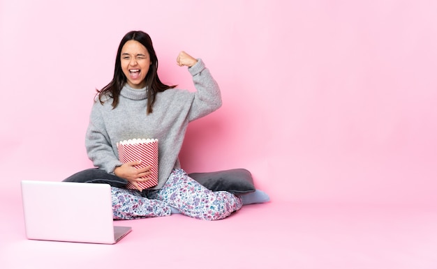 Giovane donna seduta sul pavimento e mostrando un film in un laptop