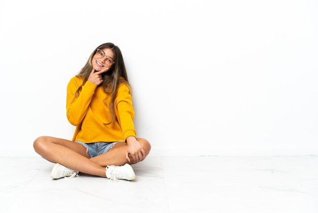 Giovane donna seduta sul pavimento isolata su sfondo bianco sorridente