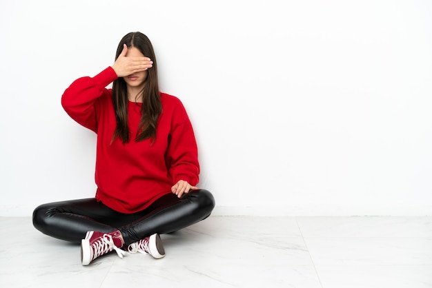 Giovane donna seduta sul pavimento isolato su sfondo bianco che copre gli occhi con le mani. Non voglio vedere qualcosa