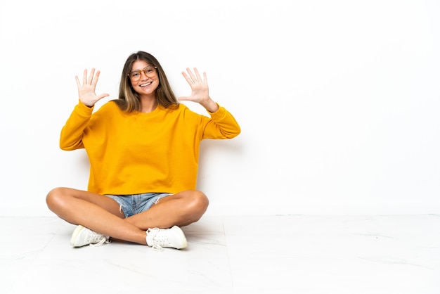 Giovane donna seduta sul pavimento isolato sul muro bianco contando dieci con le dita