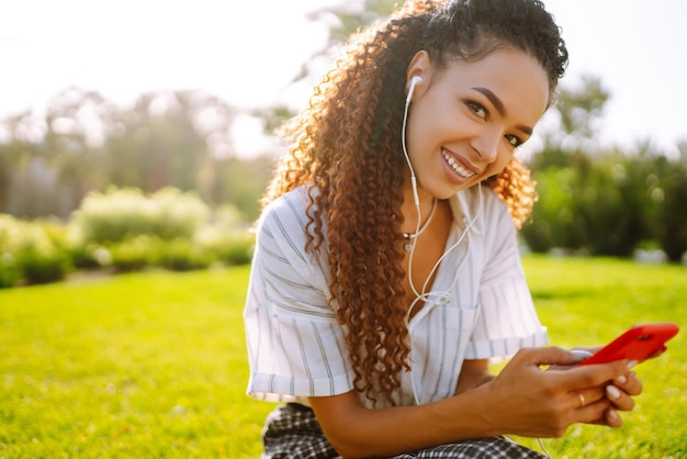 Giovane donna seduta sull'erba verde nel parco con il telefono Donna graziosa che ascolta la musica