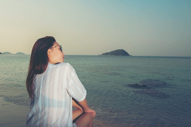 Giovane donna seduta sulla roccia sulla spiaggia