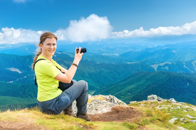 Giovane donna seduta sulla scogliera di montagne e scattare foto di viaggio sulla fotocamera