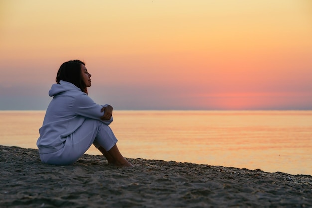 Giovane donna seduta sulla spiaggia del mare che guarda sull'alba lo spazio della copia destinazione di viaggio per le vacanze estive