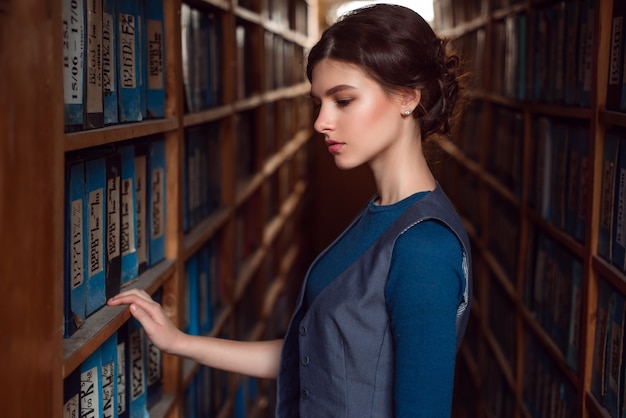 Giovane donna selezionando libro dallo scaffale della libreria.