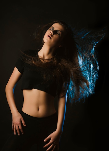 Giovane donna sensuale con capelli svolazzanti in posa in studio con luce blu