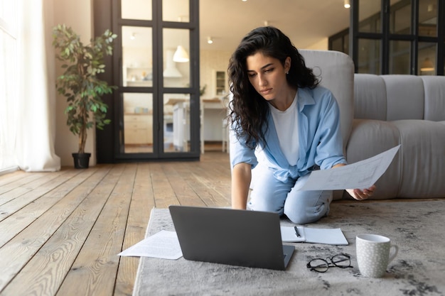 Giovane donna seria che lavora al computer portatile da casa guardando i documenti che hanno affari online