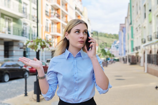 Giovane donna seria di affari che parla sul fondo della via della città del telefono cellulare