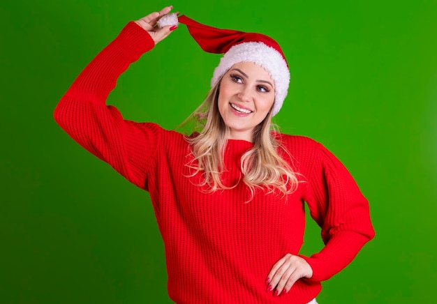 Giovane donna sexy di Capodanno con lunghi capelli biondi e bel viso in cappello rosso in vacanza di Babbo Natale in posa su sfondo verde Emozione faccia a sorpresa