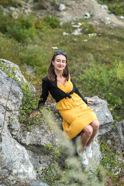 Giovane donna sexy esile che posa vicino alla grande pietra e all'erba alta verde, avventura estiva perfetta