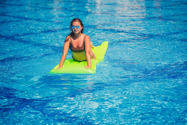 Giovane donna sexy in costume da bagno nuota in piscina su un materasso gonfiabile Ragazza in occhiali da sole con un sorriso sui volti in una piscina blu in vacanza