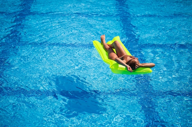 Giovane donna sexy in costume da bagno nuota in piscina su un materasso gonfiabile. Ragazza in occhiali da sole in una piscina blu in vacanza