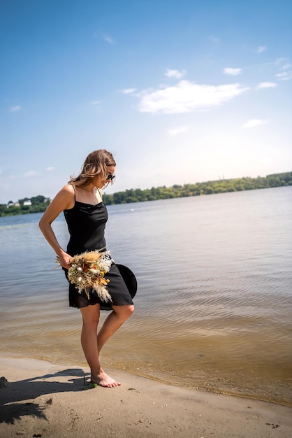 Giovane donna sexy in vestito nero che cammina della vacanza sul lago e si rilassa