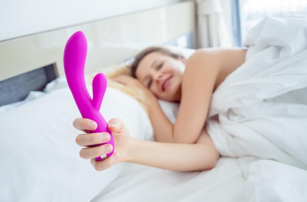 Giovane donna sexy nel letto con in mano un sex toy per adulti