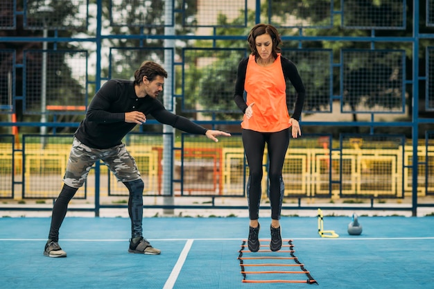 Giovane donna si esercita usando la scala di agilità lavorando con l'allenatore di fitness