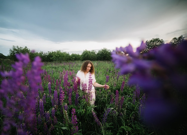 Giovane donna si trova in camicia bianca nel campo dei lupini viola e rosa