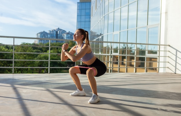 Giovane donna slim fit che si allena con elastici fitness all'aperto in città