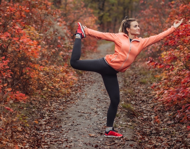 Giovane donna slim fit in abiti sportivi che praticano esercizi di yoga asana nella foresta di autunno