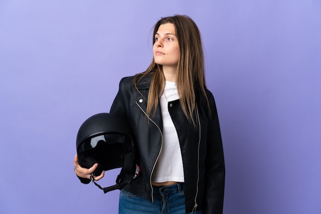 Giovane donna slovacca che tiene un casco da motociclista isolato sulla parete viola che guarda al lato