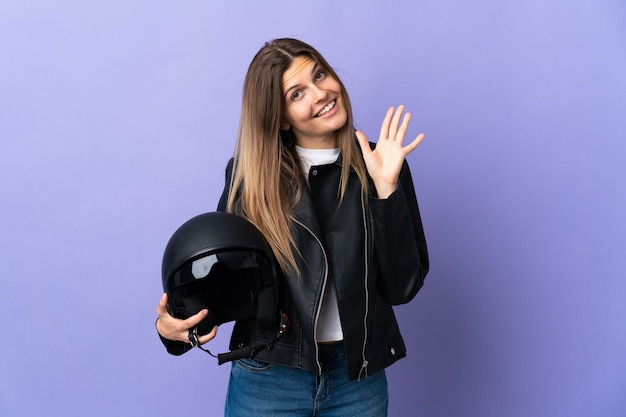 Giovane donna slovacca che tiene un casco del motociclo isolato su priorità bassa viola che saluta con la mano con l'espressione felice